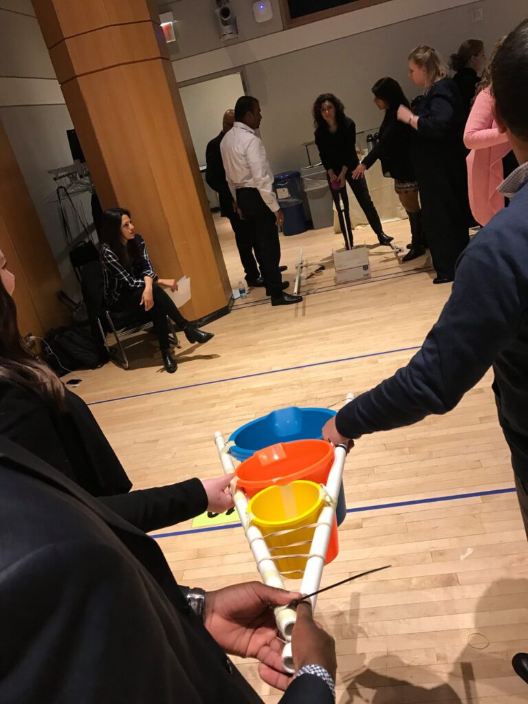 Participants in a team building activity indoors, holding a structure with colorful buckets as part of the Catapult to Success event, focusing on teamwork, coordination, and strategic planning.