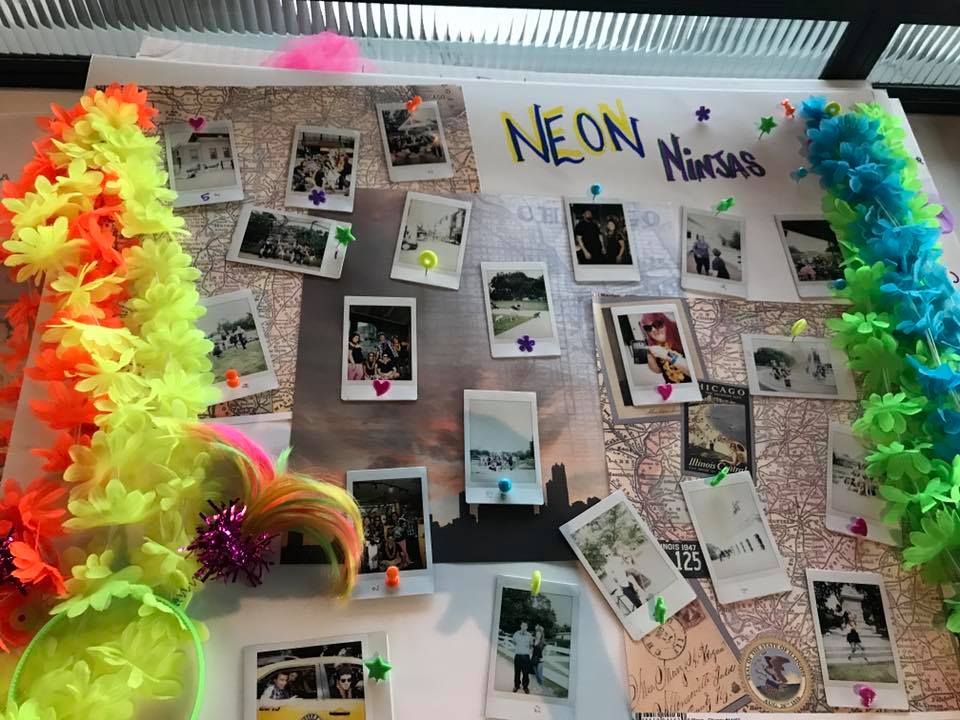A vibrant display board titled 'Neon Ninjas' from a Polaroid scavenger hunt, decorated with colorful leis and neon accents. The board features a collection of Polaroid photos pinned around a central map, capturing fun moments from the scavenger hunt challenges. The lively decorations and creative photo arrangement highlight the energy and excitement of the team building event.