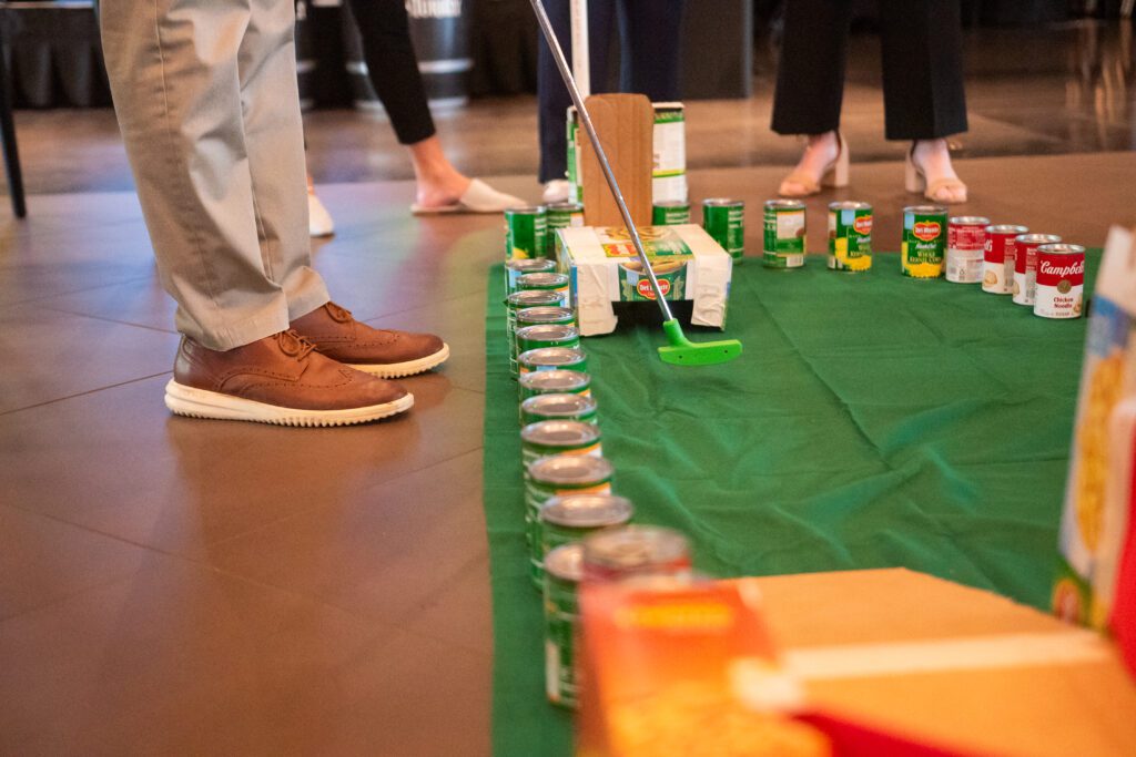 Participants play on a custom-built mini golf course made from canned goods and other non-perishable food items during a 'Build Your Own Mini Golf Course' team building event.