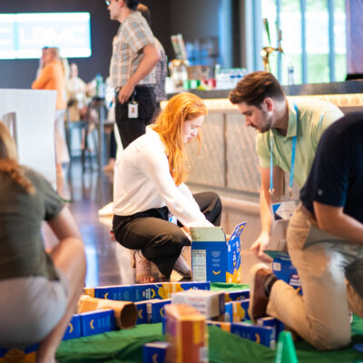 Participants collaborate to build a mini golf course using canned goods and packaged food items during a 'Build Your Own Mini Golf Course' team building event. The activity encourages teamwork and creativity, with the food items being donated to a local food pantry after the event, combining fun with a charitable cause.