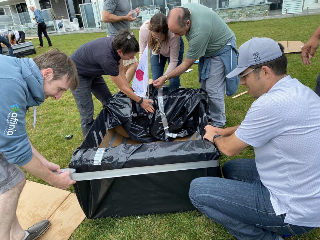 Team members collaborating to construct a cardboard boat during the Build-A-Boat team building activity.