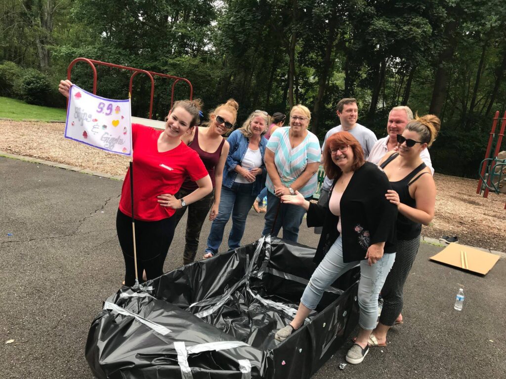 Team posing proudly next to their completed cardboard boat during the Build-A-Boat team building challenge.