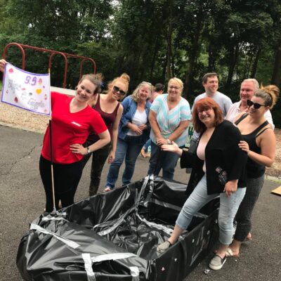 Team posing proudly next to their completed cardboard boat during the Build-A-Boat team building challenge.