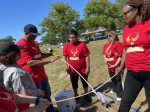 A team of participants in red shirts working together outdoors on constructing a catapult during the Catapult to Success team building activity, showcasing collaboration, creativity, and strategic planning.