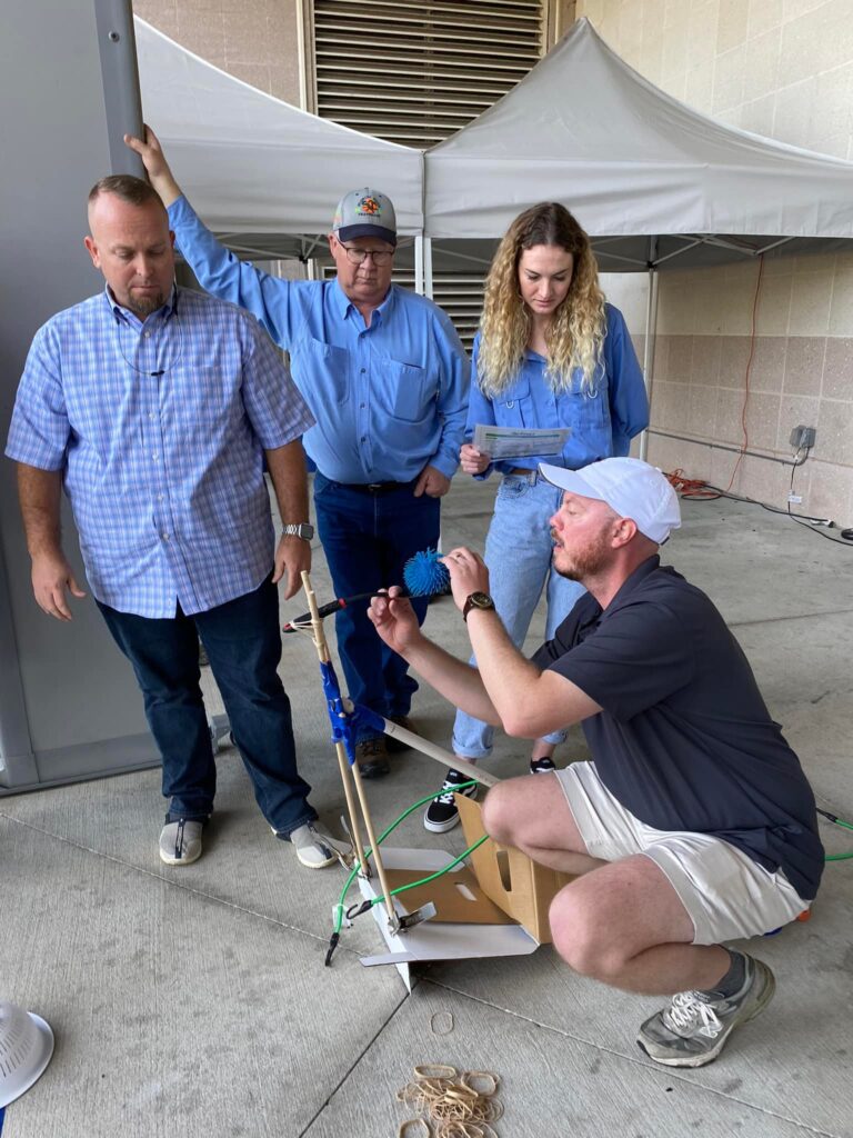 A group of four participants outdoors working together to assemble a small catapult during the Catapult to Success team building activity, emphasizing teamwork, innovation, and hands-on problem-solving.