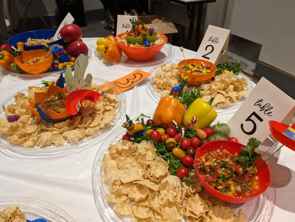 Colorful bowls of salsa and fresh ingredients, surrounded by tortilla chips and labeled for different teams during the Salsa Showdown team building event.