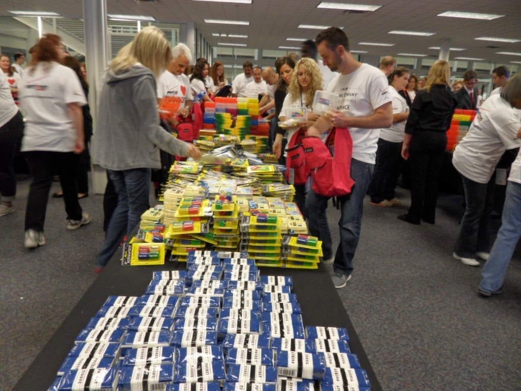 Team building participants are organizing and packing school supplies, including notebooks, pencils, and backpacks, at a Tools for Schools CSR program.