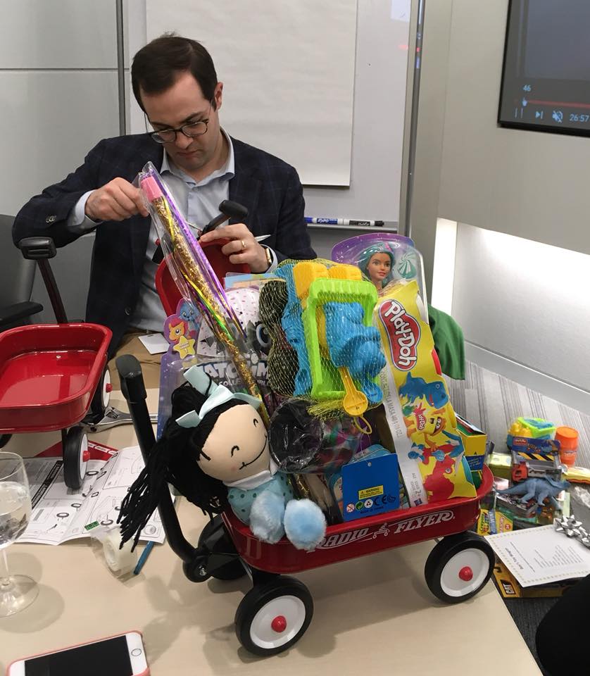 Participant assembling a wagon filled with toys during a charitable holiday team building activity.