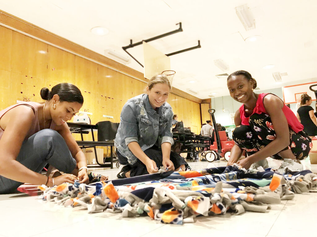 Three participants work together to craft a colorful fleece blanket during The Big Give team building event, supporting children’s charities.