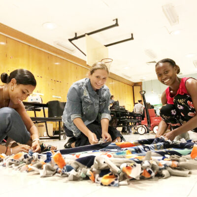 Three participants work together to craft a colorful fleece blanket during The Big Give team building event, supporting children’s charities.