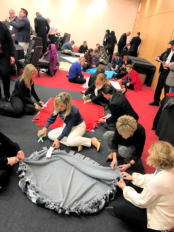Teams enthusiastically work together, crafting fleece blankets during The Big Give team building event, destined for donation to local charities.