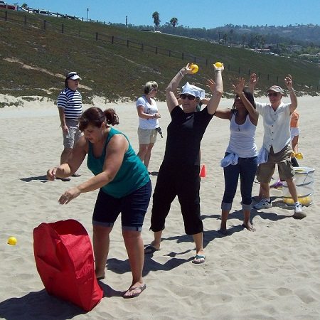 Teams competing in a fun relay race on the beach as part of a sand sculpting team building event.