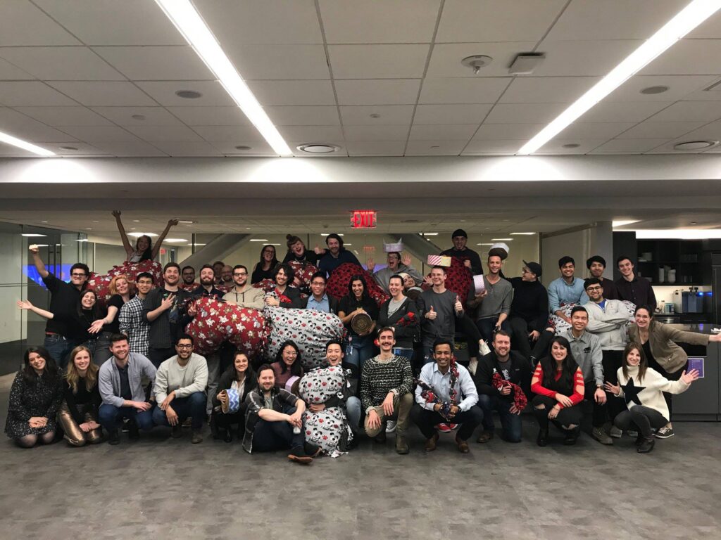 A large group of participants poses together after successfully completing the Paws For A Cause team building event, proudly displaying the dog beds and toys they made for donation to local animal shelters.