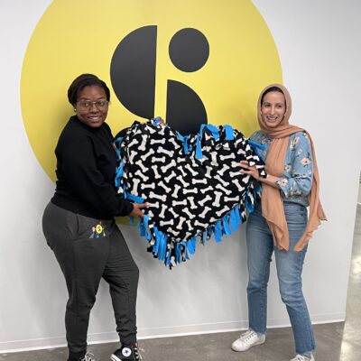 Two participants proudly display a heart-shaped dog bed they created during the Paws For A Cause team building event, supporting local animal shelters with hand-crafted donations.