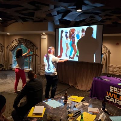 Participants engage in a lively music and dance challenge during the Wild Card Team Building Bingo event, with a vibrant video displayed on the screen.