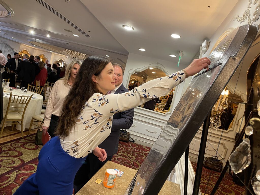 A participant enthusiastically places a marker on a large game board during the Foodbank Showdown team building event. The activity combines friendly competition with a charitable purpose, helping local families in need.