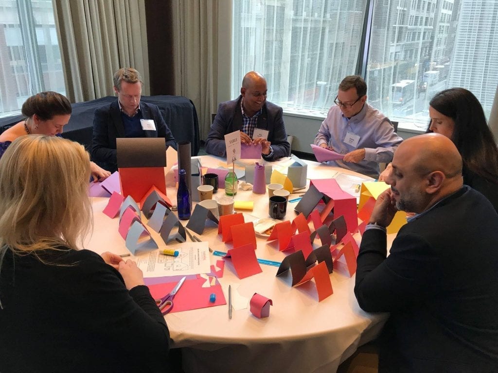 Participants sit around a table working together on assembling personal care kits during the Helping Hands team building event.
