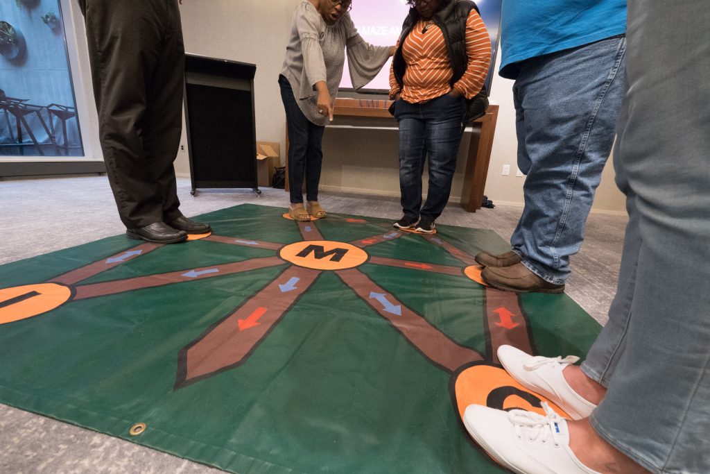 Participants engaging in an interactive Team and Leadership DNA activity, using a large, colorful floor mat designed to explore key team dynamics and enhance communication.