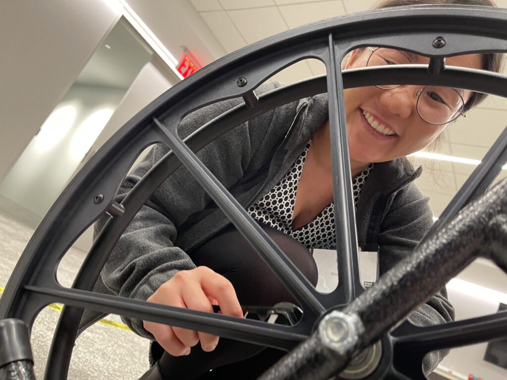A participant smiles while working on assembling a wheelchair during a team building event for charity. The Wheelchairs In Motion activity involves building wheelchairs to donate to veterans and those in need.