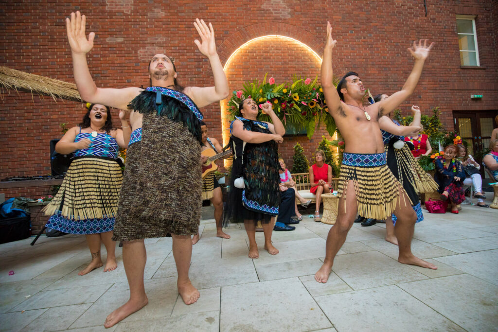 Maori performers in traditional dress energetically lead a Haka team building session, inspiring participants with chants and powerful movements.