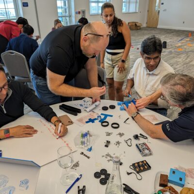 A group of participants is working together to assemble a robot. The table is filled with parts, tools, and instructions as they collaborate during a robotics team building event.