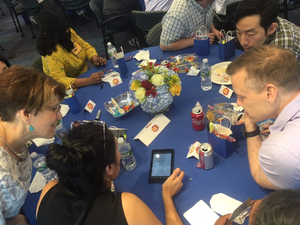 Team members huddle around a table, strategizing answers during a high-energy Corporate Quiz Bowl team building challenge.