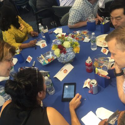 Team members huddle around a table, strategizing answers during a high-energy Corporate Quiz Bowl team building challenge.