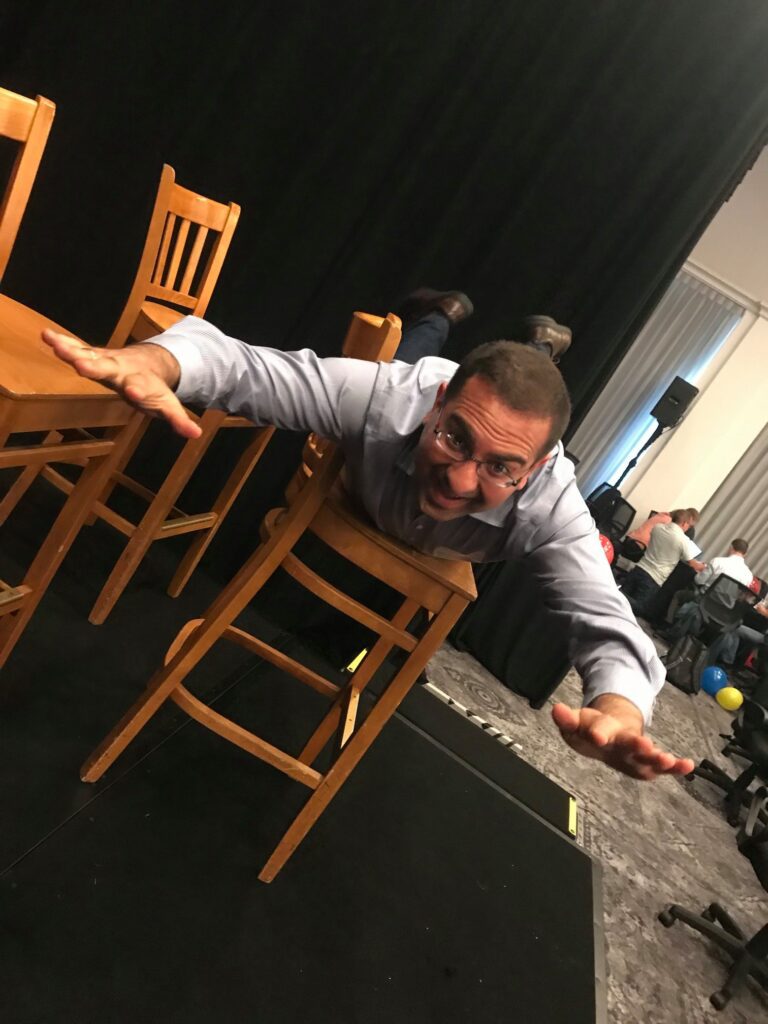 A participant fully embraces the fun and physical aspect of the game, executing a dramatic chair stunt while surrounded by a team engaged in the lively atmosphere. This highlights the playful, energetic spirit of the event.