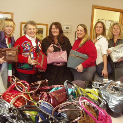 Participants proudly display gently-used handbags collected for donation at a Hopefull Handbags Global team building event, supporting survivors of domestic abuse.