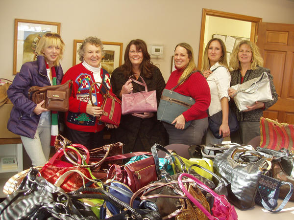 Participants proudly display gently-used handbags collected for donation at a Hopefull Handbags Global team building event, supporting survivors of domestic abuse.