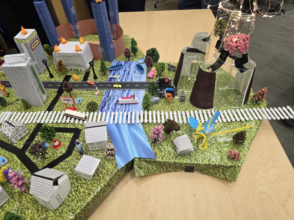 Close-up of a detailed miniature city model featuring buildings, roads, trees, and waterways created during the City Build team building event.