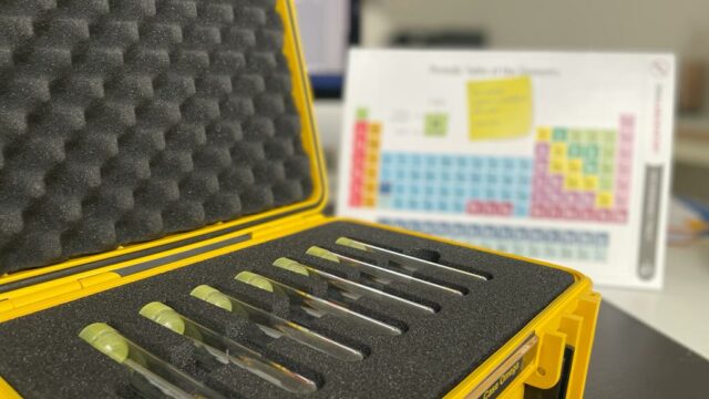 Close-up of a yellow case holding test tubes, with a periodic table in the background, used as part of the 'Atmosphere' team building event.