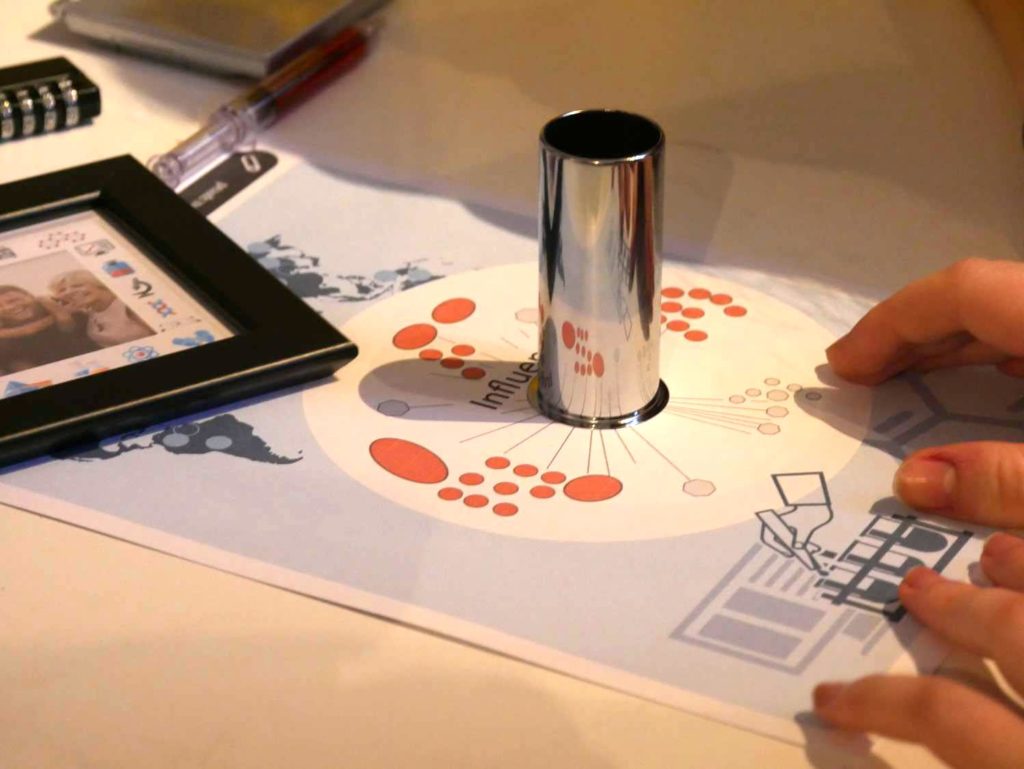 Participant solving a puzzle by using a reflective cylinder on a diagram during the 'Atmosphere' team building event.