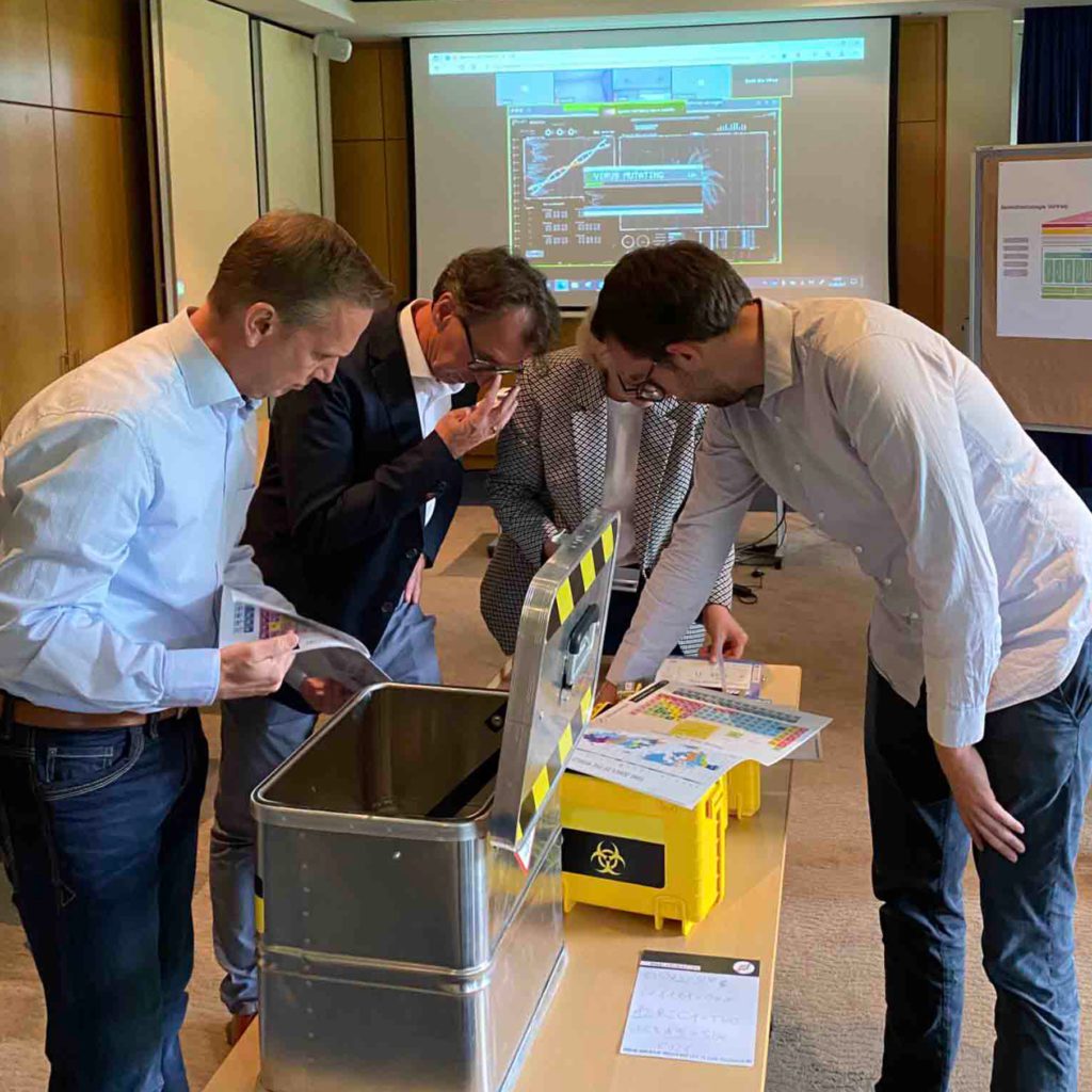 Group of participants analyzing documents and tools around a biohazard-themed box as part of the 'Atmosphere ' team building activity.