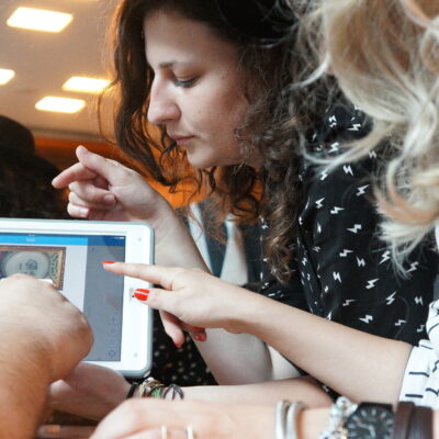 Three people closely examining a clue on a tablet screen during the 'Escape the Mob' team building activity. They are focused and engaged in solving a mystery, collaborating to piece together information and create a strategy for the game.