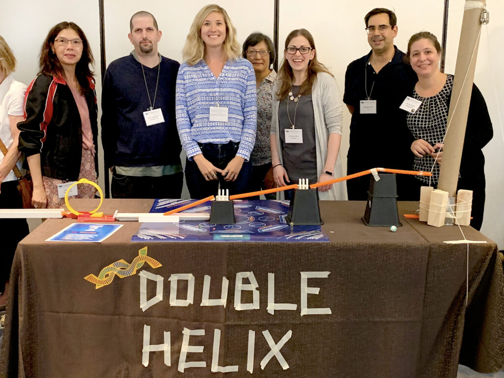 Team stands behind their completed 'Double Helix' themed chain reaction machine, showcasing their collaborative creation at a team building event.