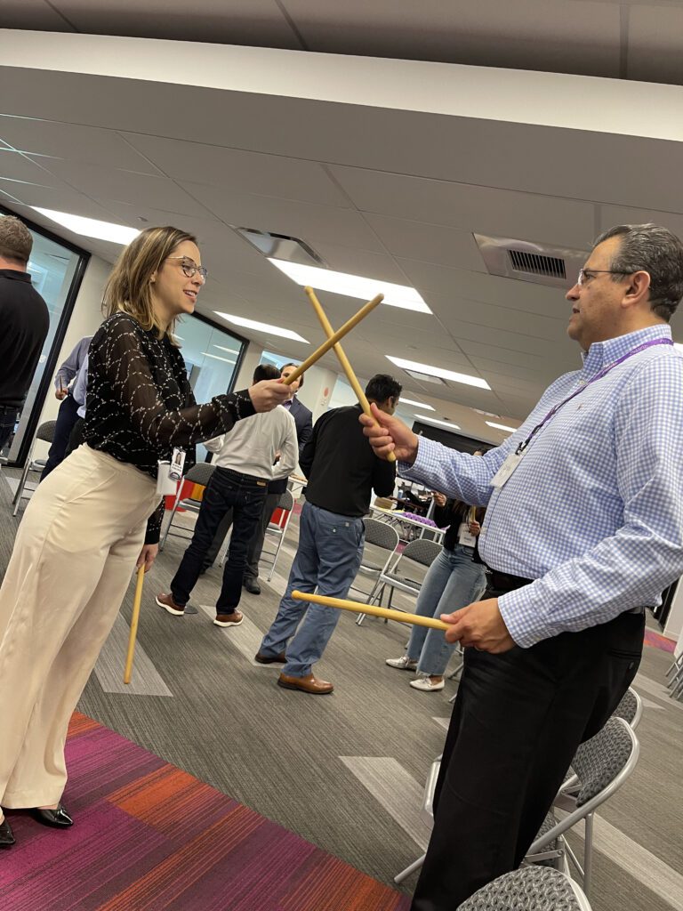 Two participants practicing rhythm coordination with drumsticks during a BeatsWork team building activity.