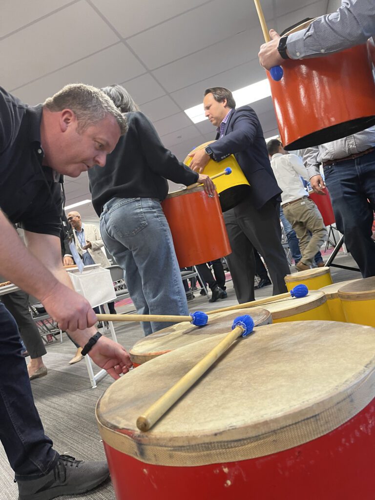 Participants engaged in a drumming session, playing large percussion drums during a BeatsWork team building activity.