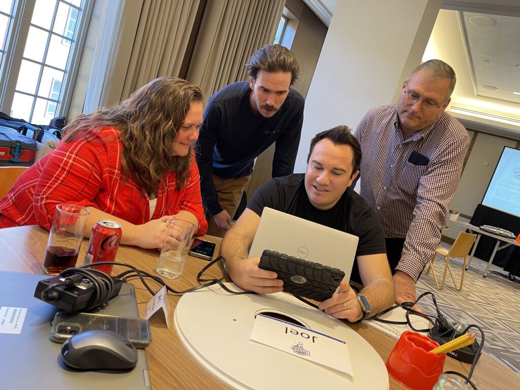 A group of four team members are looking at a tablet during the Wheels Around the World team building event.