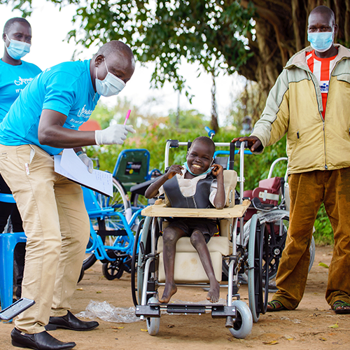 A smiling child in a wheelchair, sponsored by the Wheels Around the World team building event, receives care and attention from team members.