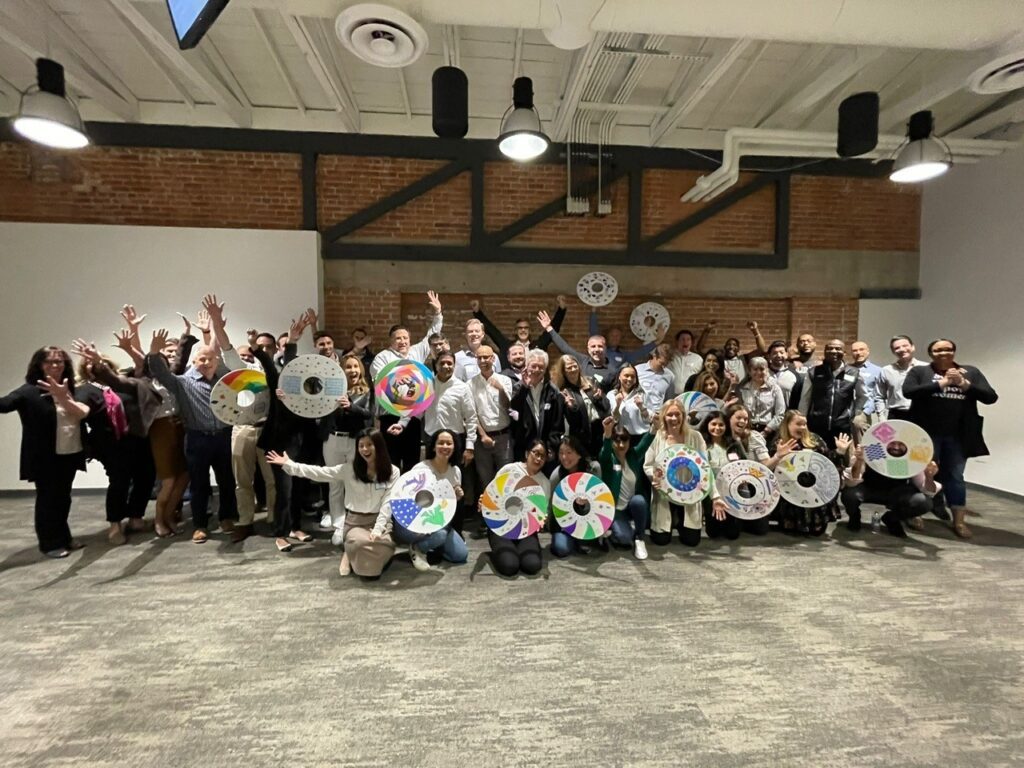 A large group of participants proudly display their decorated wheel safety covers during the Wheels Around the World team building event, celebrating their contribution to providing wheelchairs for individuals in need.