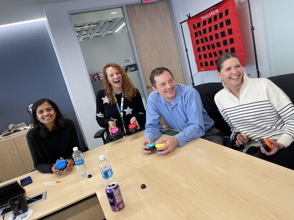 A group of colleagues smiling and engaging in a fun game during a team building event, with colored buzzers in hand and a target game board in the background.