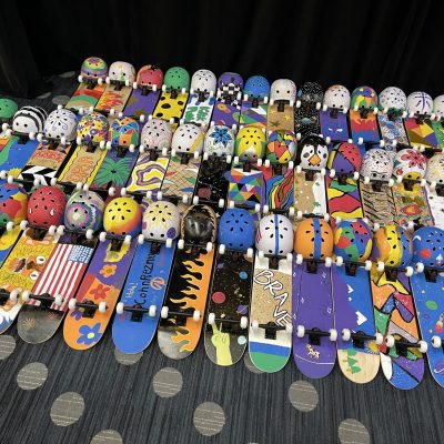 A vibrant display of decorated skateboards and helmets created during the Just Roll With It team building event, showcasing the creativity and teamwork of participants.