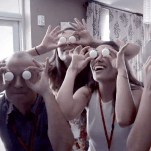 Team members having fun during a playful Quickfire Halloween challenge, using ping pong balls as pretend spooky eyes for a lighthearted moment.